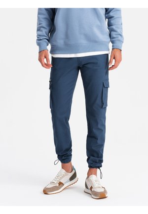 Marinblå cargo-byxor med elastiska muddar, featuring sidofickor och en slät yta. Kombinerat med mångfärgade sneakers och en ljusblå sweatshirt.