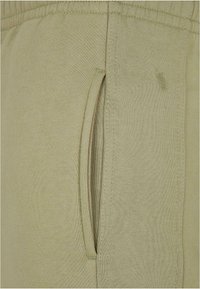 Light green jogger pant fabric featuring a side slit pocket with ribbed waistband. The texture is smooth and soft, with a clean finish.