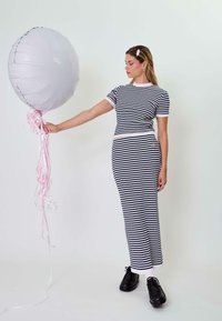Svītrainas kleitas, tumši zilā un baltā, pieguļošs augšdaļa, gara svārki, apvienota ar melnām kurpēm. Modelis tur lielu sudrabotu balonu ar rozā lentēm.
