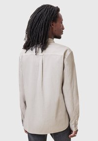 Lichtbeige langemouwen shirt met een gladde textuur, plooidetail op de rug, knoopmanchetten en afgeronde zoom.