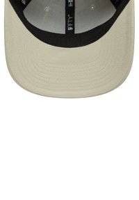 Beige cap with a black bill, featuring a smooth fabric texture. Inside, a grey lining with printed branding. Structured design, flat brim.