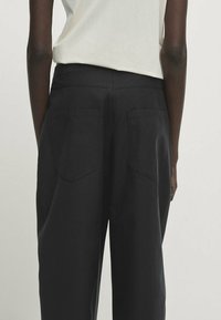 Czarne, wysokie spodnie wykonane z mieszanki bawełny, z dwiema tylnymi kieszeniami, prostymi nogawkami i minimalnymi detalami przeszycia.