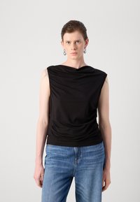 Svart ermeløs topp med drapert stoffdesign, glatt tekstur og tettsittende kant. Kombinert med blå jeans, vist mot en ensfarget bakgrunn.