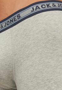 Grijze katoenen boxershorts met een marineblauwe tailleband waarop "JACK & JONES" in het blauw is gedrukt. Zachte textuur met een snug fit.