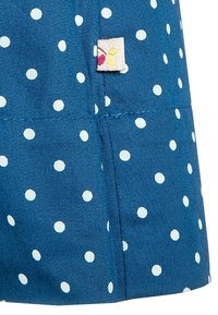 Niebieska tkanina w białe kropki, z małą metką z stylizowanym wzorem liścia. Gładka tekstura, materiał o średniej wadze.