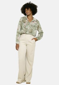 Green and light pink patterned shirt with long sleeves and a collar, paired with beige wide-leg trousers. Casual and relaxed fit.