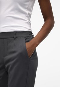 Pantalons gris ajustés avec une taille élastique, poches latérales et une texture lisse, associés à un débardeur blanc à côtes.