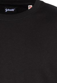 Sudadera negra de cuello redondo hecha de tela suave, con cuello acanalado y una pequeña etiqueta con detalle de la bandera estadounidense.