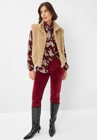 Beige nepdonsvest over een gebloemd rood en crèmekleurig blouse, gecombineerd met bordeaux corduroy broek en zwarte kniehoge puntige laarzen.