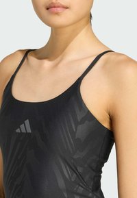 Zwart atletisch zwemkleding met dunne bandjes, voorzien van een textuurpatroon en een reflecterende logo op de borst. Glad stof.
