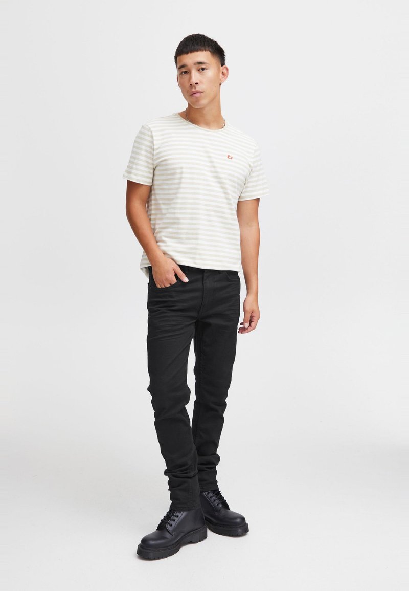 Bež s črtami in bela majica s kratkimi rokavi, črne oprijete jeans hlače in črni škornji. Na majici je majhen logotip na prsih.