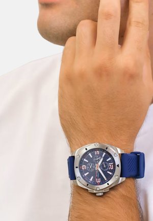 Montre de sport avec un bracelet en silicone bleu marine et un boîtier en acier inoxydable. Présente un cadran sombre, des index blancs et des accents rouges.