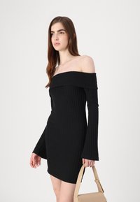 Vestido preto de malha canelada, com decote off-shoulder, mangas longas e uma silhueta ajustada. Apresenta um design de malha texturizada e um decote alto.