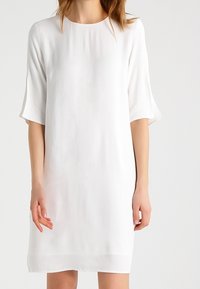Vestido blanco de manga corta con un corte holgado, escote redondo y tela ligera, que presenta una sutil textura y un dobladillo recto.