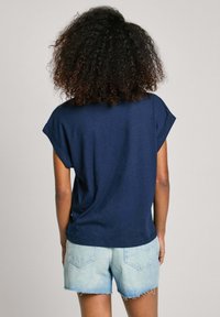 Tamsiai mėlyna trumpa rankovė t-shirt su sukrautomis rankovėmis, derinama su šviesiais džinsiniais šortais su nuskandintais kraštais ir užpakalinėmis kišenėmis.