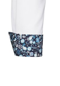 Camicia bianca con polsini a motivi blu navy che presentano disegni floreali e paisley in tonalità di blu e turchese, evidenziando dettagli intricati.