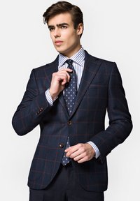 Granatowy blazer w kratę z fakturowanej tkaniny, z brązowymi guzikami, nałożony na koszulę w paski i krawat w kropki.