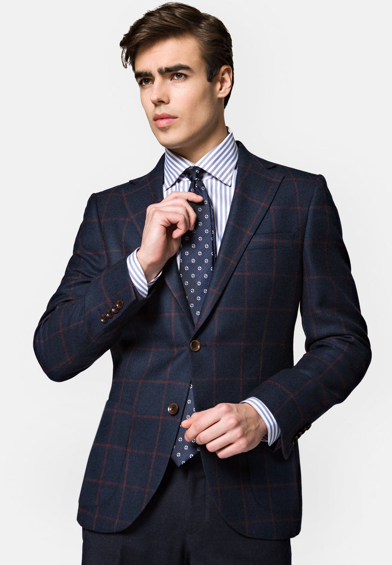 Granatowy blazer w kratę z fakturowanej tkaniny, z brązowymi guzikami, nałożony na koszulę w paski i krawat w kropki.