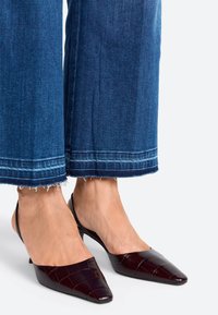 Pailgi, bordo spalvos slingback batai su tekstūruotu krokodilo raštu ir žemu kulnu, derinami su nutrintomis kulkšninių džinsais.