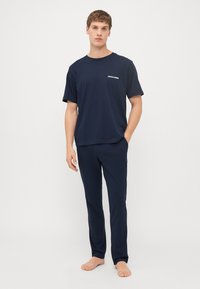 Marineblå bomulds T-shirt med korte ærmer og rund halsudskæring, med et hvidt logo. Sammen med matchende marineblå bukser.