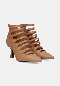 Botas de tobillo de cuero marrón con correas ranuradas y acentos de botones, punta afilada y un tacón de aguja de 3 pulgadas. Textura suave, diseño moderno.
