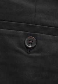 Gros plan d’un tissu noir avec un bouton brillant à quatre trous cousu sur le matériau près d’une ligne de couture.