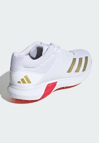 White athletic shoe with breathable mesh upper, gold striped accents, red sole, and integrated lacing system for secure fit and support.