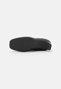 Zapato negro con un empeine de cuero suave, punta redonda, tacón bajo y suela de goma texturizada. Diseño simple sin adornos visibles.