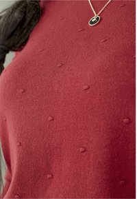 Bordó pletený svetr se strukturovaným vzorem s malými vystouplými tečkami, doplněný jemným zlatým náhrdelníkem s kruhovým přívěskem.