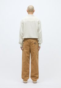 Φωτεινό πουκάμισο με ριγέ σχέδιο και μακριά μανίκια, συνδυασμένο με χαλαρές, ανοιχτό καφέ cargo παντελόνες. Τα παντελόνια διαθέτουν τσέπες και ετικέτα με λογότυπο στο πίσω μέρος.