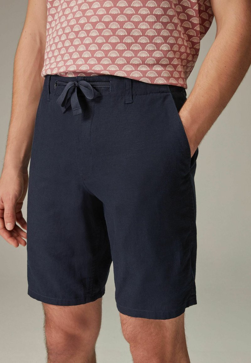 Shorts din in bleu marin, din in, cu talie cu șnur, buzunare laterale și o croială lejeră, evidențiind o textură netedă și respirabilă.