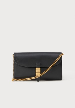 Clutch in pelle nera con patta pieghevole, tracolla in catena dorata e un accento decorativo dorato con lettere in rilievo, texture liscia.