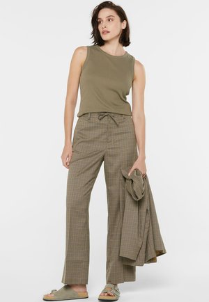 Olivgrünes ärmelloses Top, karierte weite Hosen mit Kordelzug und graue Rutsch-Sandalen. Das Outfit hat klare Linien und weiche Texturen.