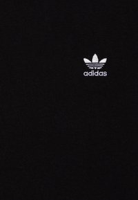 Svart bomull T-skjorte med et lite brodert Adidas-logo i hvitt med trefoil-design. Stoffet er glatt med minimal tekstur.