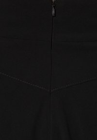 Schwarze hochtaillierte Hose mit Reißverschluss, aus strukturiertem Gewebe und kontrastierenden Nähten in einem dreieckigen Design auf der Rückseite.