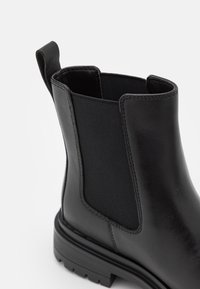 Botín negro de piel con paneles laterales elásticos, una superficie texturizada y una suela de goma duradera con un tacón bajo.