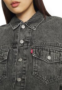 Giacca di denim grigia con colletto classico, due tasche sul petto, bottoni automatici argentati e una linguetta rossa Levi's sulla tasca sinistra.