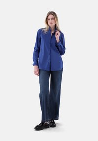 Blue long-sleeve button-up shirt with a collar, paired with wide-leg dark denim jeans and black platform shoes. Smooth fabric and casual fit.
