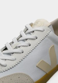 Λευκό πάνινο αθλητικό παπούτσι με μπεζ δερμάτινες λεπτομέρειες, λευκά κορδόνια, υφασμένο λαστιχένιο πάτο και εμφανές λογότυπο V στο πλάι.