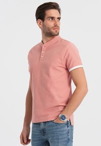 Polo shirt rosa in cotone a maniche corte con colletto a bottone e dettagli bianchi sulle maniche. Indossato con jeans in denim blu.