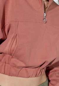 Felpa rosa con zip a metà, realizzata in tessuto testurizzato, dal design cropped, con orlo elasticizzato e tasche laterali per funzionalità.