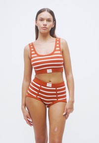 Κόκκινο κοντό τοπ με ριγέ λευκές οριζόντιες ρίγες και ταιριαστά ψηλόμεσα σορτς, με λογότυπο στο ελαστικό της μέσης.