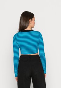 Haut court à manches longues bleu et noir avec des rayures horizontales et une texture côtelée, associé à un pantalon noir taille haute.