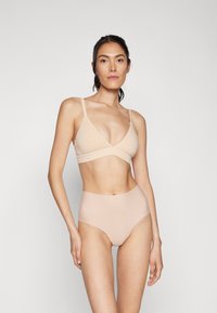 Reggiseno color carne con design triangolare e spalline sottili regolabili, abbinato a mutandine a vita alta e senza cuciture dello stesso colore.