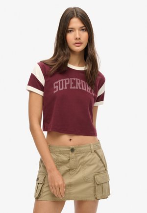 T-shirt cropped bordeaux avec des accents crème et imprimé "SUPERDRY", associée à une jupe cargo beige avec des poches latérales et une fermeture à boutons.