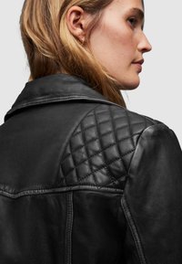 Giacca in pelle nera con dettagli trapuntati sulle spalle, texture morbida e design del colletto classico. Senza hardware visibili o abbellimenti.