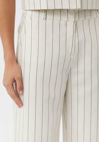 Light-colored striped trousers featuring narrow, dark vertical lines, a flat front, and side pockets, made from a textured fabric.