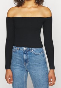 Svart ribbad off-shoulder topp med långa ärmar, i kombination med högmidjade blå denimjeans. Slät textur, figurnära siluett.