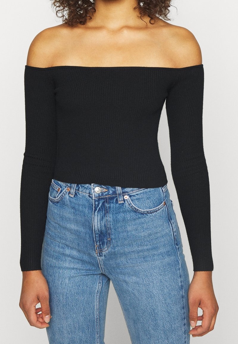 Svart ribbad off-shoulder topp med långa ärmar, i kombination med högmidjade blå denimjeans. Slät textur, figurnära siluett.
