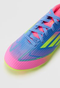 Soccer cleat with a blue, pink, and green gradient design; features a textured surface, flat laces, and prominent branding on the side.